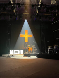 Eine leere Bühne zur Mehr-Konferenz in Augsburg. Im Scheinwerferlicht ist ein Kreuz zu sehen.